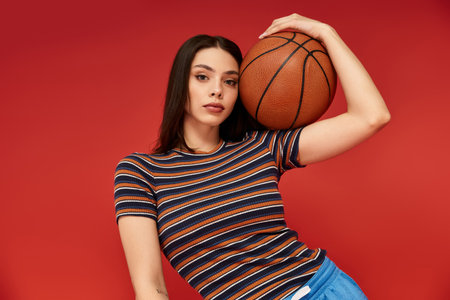 A beautiful woman poses confidently against a striking red background while holding a basketball.
