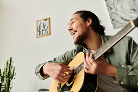 A handsome young man enjoys playing his guitar at home, filled with a relaxed and cheerful mood.