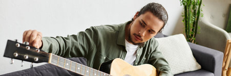 A young handsome man meticulously tunes his acoustic guitar in a comfortable home setting.