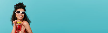 A cheerful young woman in stylish sunglasses sips a colorful drink, radiating warm summer energy.の写真素材