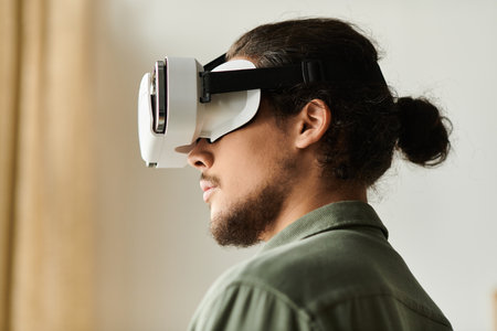 A young handsome man is deeply focused on an immersive virtual reality activity at home.