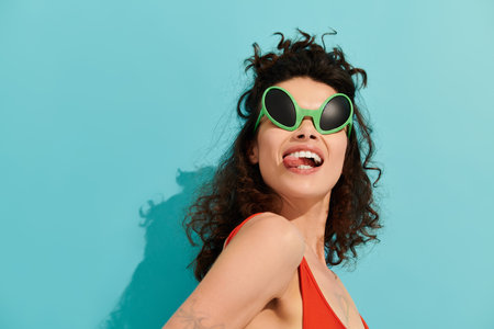A stylish woman poses playfully against a bright blue backdrop, flaunting her cool sunglasses.の写真素材