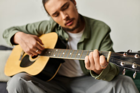 A young man strums his guitar at home, lost in the joy of music and creativity.