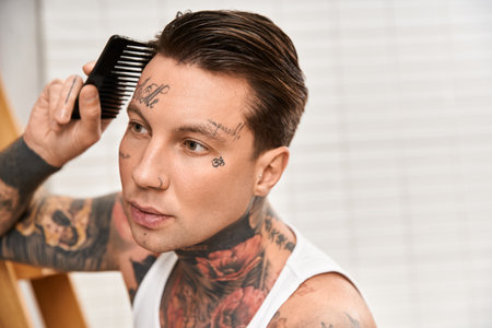 A young man with tattoos styles his hair while feeling comfortable at home in a cozy atmosphere.の写真素材