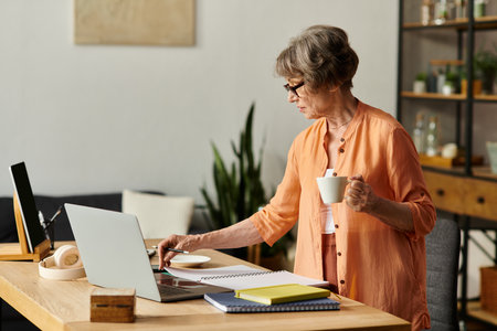 Senior woman in cozy attire engages in creativity at home while sipping tea and taking notes.の写真素材