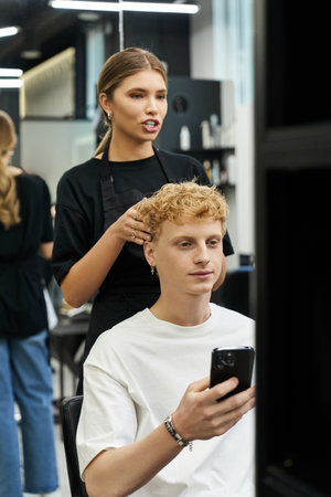 A stylist enhances a clients look while he enjoys his phone in a modern beauty salon setting.の写真素材