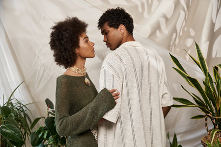 A stylish couple stands close together, surrounded by greenery, exuding love and connection.