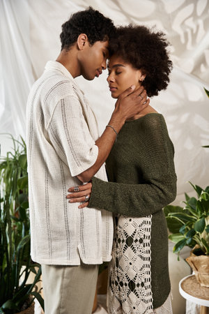 In a cozy space filled with plants, a young couple embraces tenderly, lost in their love.の写真素材