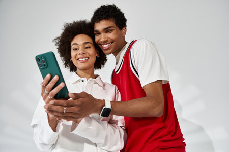 Stylish pair shares a joyful moment as they glance at their smartphone with smiles.