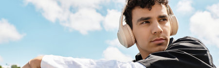 Young man at a park listens to music, enjoying the sunlight and peaceful surroundings.