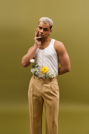 Young man poses confidently in a tank top, embracing fashion with flowers in a studio setting.