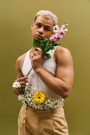 A stylish young man with dyed hair poses with vibrant flowers, exuding modern fashion in a studio.の写真素材
