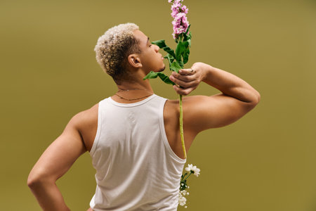 A young African American man flaunts his fashion sense in a tank top, posing with flowers.