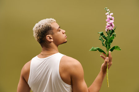 A young African American man shows off his trendy style while holding flowers in a studio.の写真素材