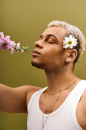 A fashionable young man poses gracefully with flowers in a studio, showcasing his unique style.