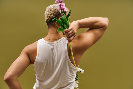 A fashionable young man showcases unique dyed hair while holding vibrant flowers in a studio.