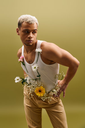 A young African American man dressed in a tank top poses gracefully with flowers in a studio.の写真素材