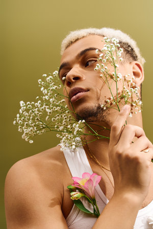 A young African American man showcases trendy fashion with dyed hair and flowers in a studio.の写真素材