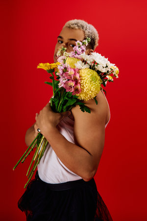 A stylish young man showcases his dyed hair while holding a bouquet of flowers in a red background.の写真素材
