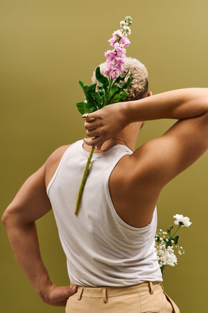 A youthful african american man poses confidently with fresh flowers, displaying a trendy look.の写真素材