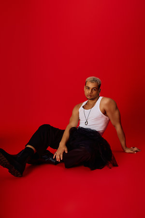 A stylish young African American man poses confidently against a vivid red backdrop, exuding charm.