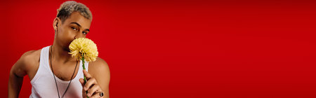 A young African American man poses playfully with a flower against a vibrant red background, bannerの写真素材