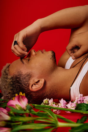 A young African American man with dyed hair poses in a striking red studio surrounded by flowers.の写真素材