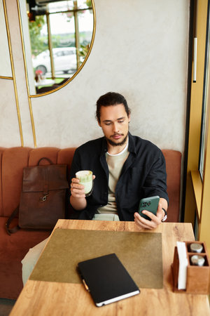 Young man with a beard balances remote work and relaxation in a vibrant cafe during summer.の写真素材