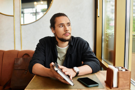 Young man with a beard sitting at a serene cafe during summer days.