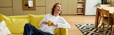 Bright and cheerful atmosphere as a young man lounges on a yellow sofa, sipping from his cup.の写真素材
