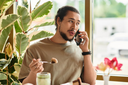A young man with a beard works remotely in a cafe while enjoying matcha and cake.の写真素材