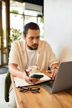 A young man with a beard works diligently on his laptop while sipping coffee in a warm cafe.