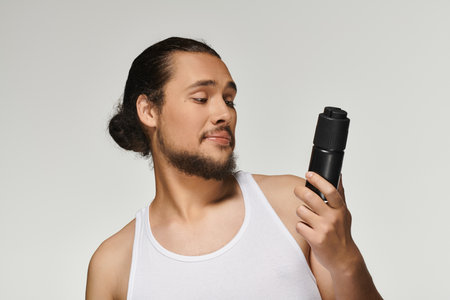 Focused young man with beard admires a grooming product under bright studio lights.の写真素材
