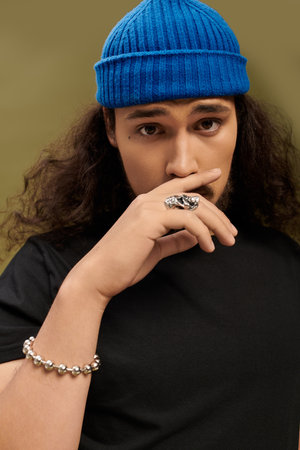 A stylish young bearded man poses confidently, showcasing his unique accessories and fashion.