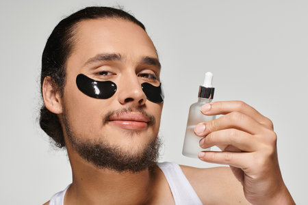 Young bearded man enjoys self care ritual with serum and eye patches for a fresh look.の写真素材