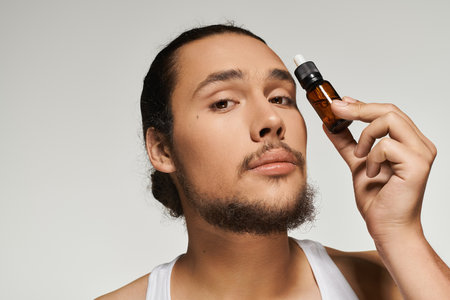 Young man with a beard holds skincare oil bottle, showcasing a confident expression in studio.の写真素材