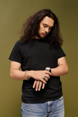 Young bearded man gazes at his watch, showcasing a laid back style and thoughtful demeanor.