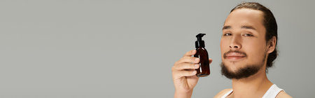Confident young bearded man holds a grooming product against a simple backdrop, highlighting style.