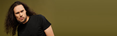 A bearded young man stands confidently, playfully posing against a soft backdrop.の写真素材