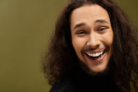 A handsome young bearded man smiles warmly, exuding charisma and confidence in a lively environment.
