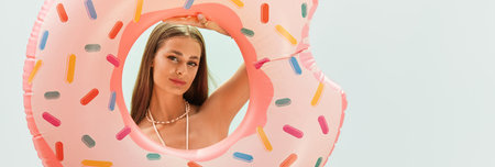 A young woman radiates joy as she poses with a colorful inflatable donut in bright summer sunlight.