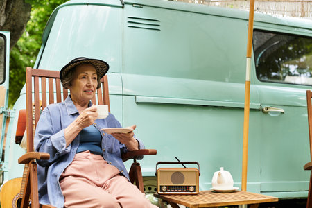 A senior woman relaxes in her garden, savoring tea while surrounded by natures beauty.の写真素材
