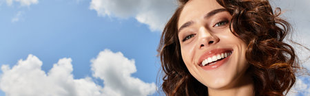 A pretty young woman with wavy brown hair smiles brightly outdoors on a sunny summer day, bannerの写真素材