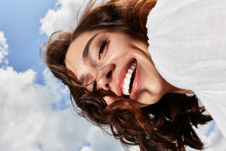 A young woman with wavy brown hair enjoys a joyful summer day under a clear blue sky.の写真素材