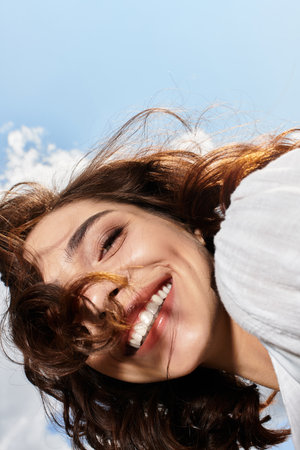 A young woman with wavy brown hair beams with happiness on a sunny summer day outdoors.の写真素材