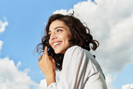A pretty young woman enjoys a sunny summer day outdoors, smiling against a vibrant blue sky.の写真素材