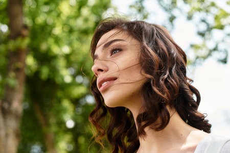 Bright sunlight illuminates a pretty young woman with wavy brown hair as she enjoys nature outdoors.