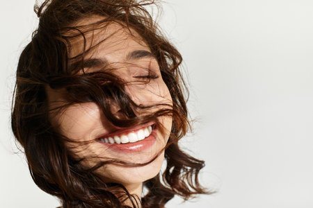 Young woman with stunning makeup smiles joyfully, her hair dancing in the studio light.の写真素材