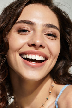 A young woman poses gracefully in a studio, showcasing her lovely makeup and bright smile.