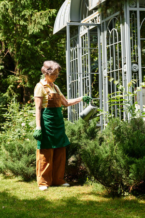 A senior woman lovingly waters her vibrant garden, surrounded by lush greenery and blooms.の写真素材